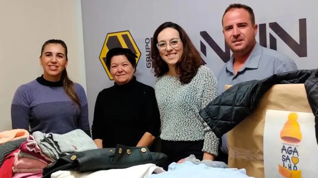 Quatro pessoas ao lado de roupas arrecadadas na Campanha do Agasalho, diante de painel com o logotipo da Santin