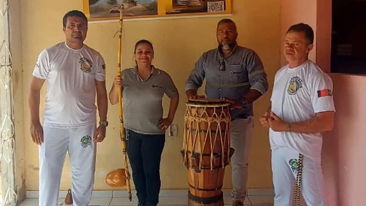 Integrantes de grupo de capoeira com atabaque ao lado de colaboradora da Santin