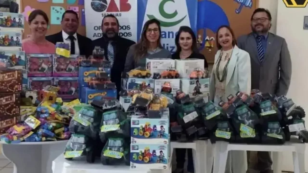 Equipe reunida atrás de mesa com brinquedos doados, em sala com painéis com as siglas OAB e PAIF