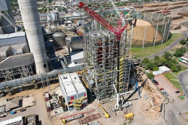 Vista aérea da caldeira de biomassa em montagem na CMPC, com guindaste de treliça vermelho ao lado da estrutura e o parque fabril ao fundo