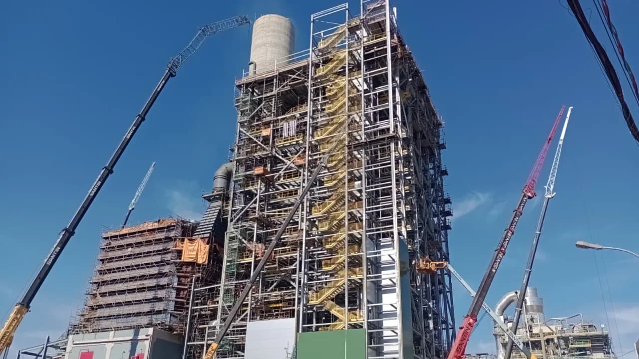 Estrutura da caldeira da CMPC com guindastes de grande porte trabalhando ao lado da fachada verde, sob céu azul