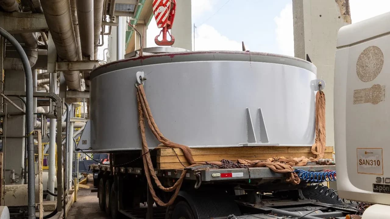 Tanque metálico de grande diâmetro sobre carreta, preso ao gancho do guindaste, na fábrica da Klabin