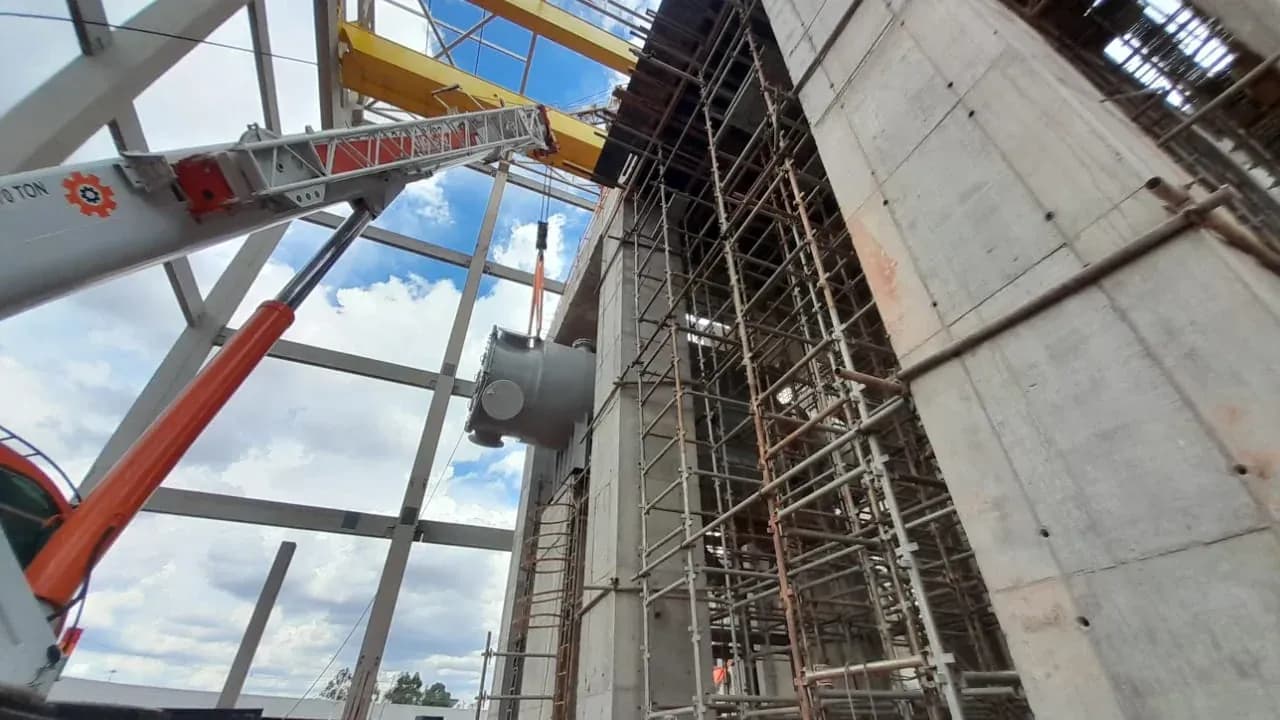 Guindaste trabalhando entre a estrutura metálica e as paredes de concreto da URE Barueri, com a ponte rolante amarela no alto