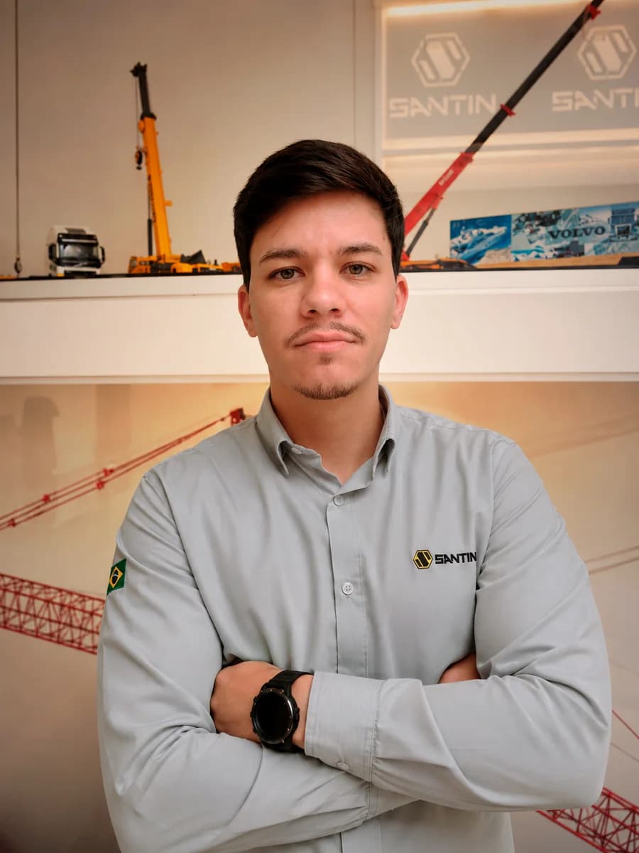 Rafael Derencio Camargo Pereira, de braços cruzados, diante do painel com guindastes da Santin